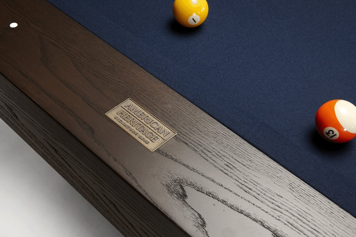 A close-up of the American Heritage logo on the Deerfield slate billiard table in a Brushed Walnut finish.